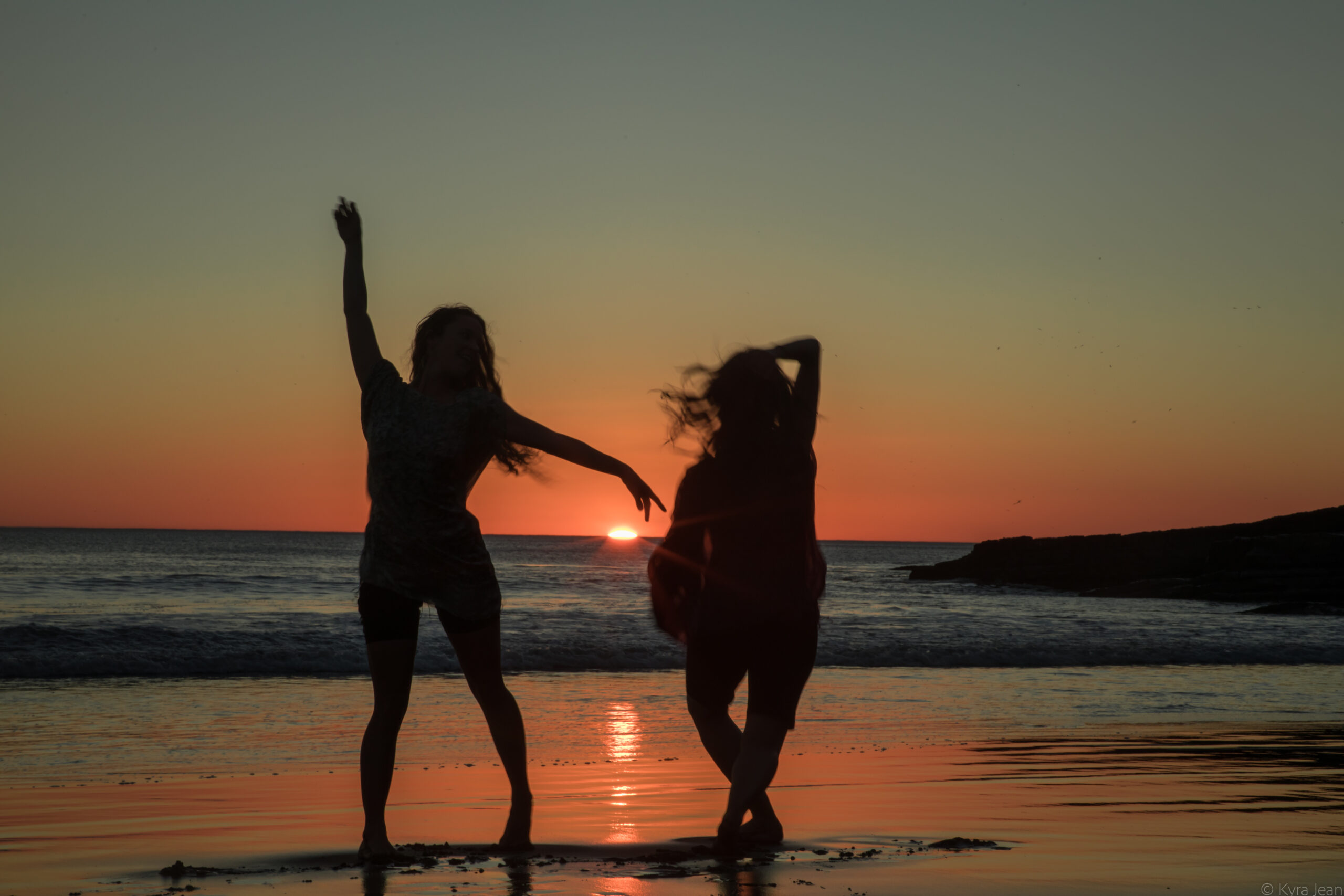 Empowered female participants on the beach at sunset, standing before the ocean and energetically greeting the sun.