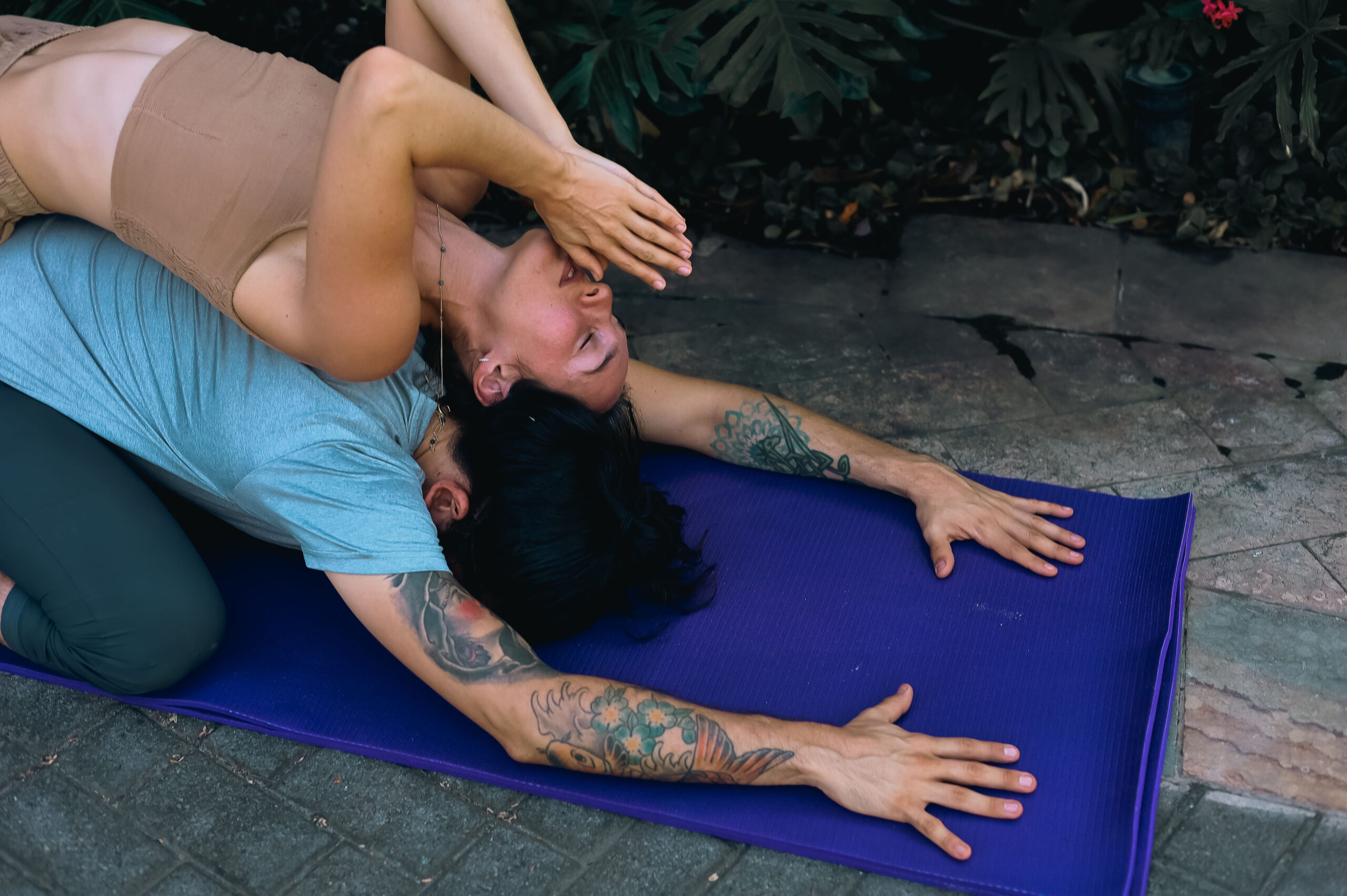 Male partner folds into child's pose while Toby Israel reclines in prayer, back to back, in a partner-yoga flow sequence.